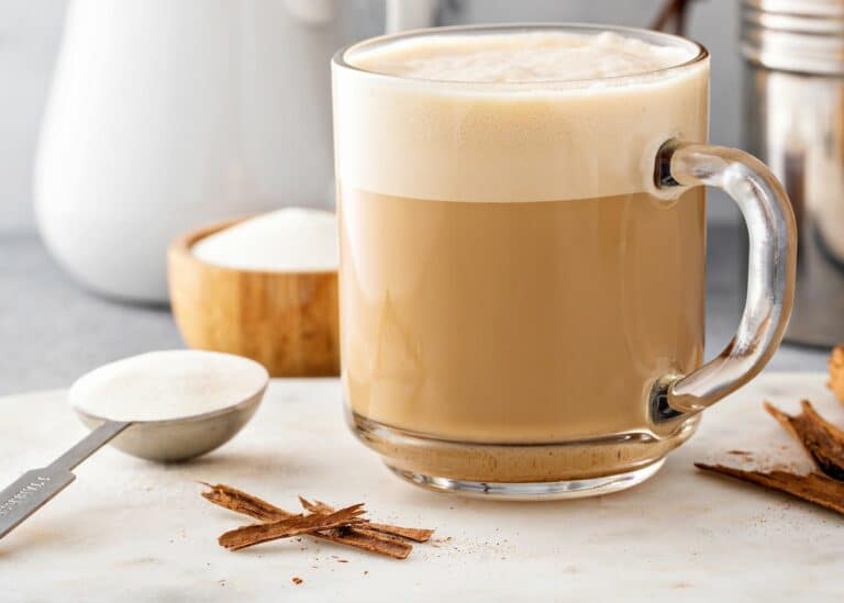 A clear glass mug of protein coffee topped with foam.