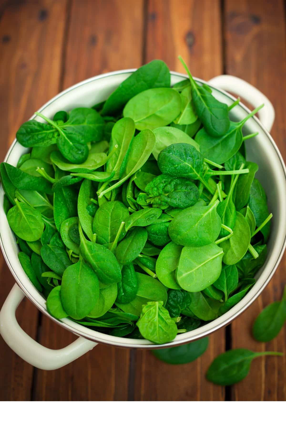 Bowl of fresh spinach on wooden surface.