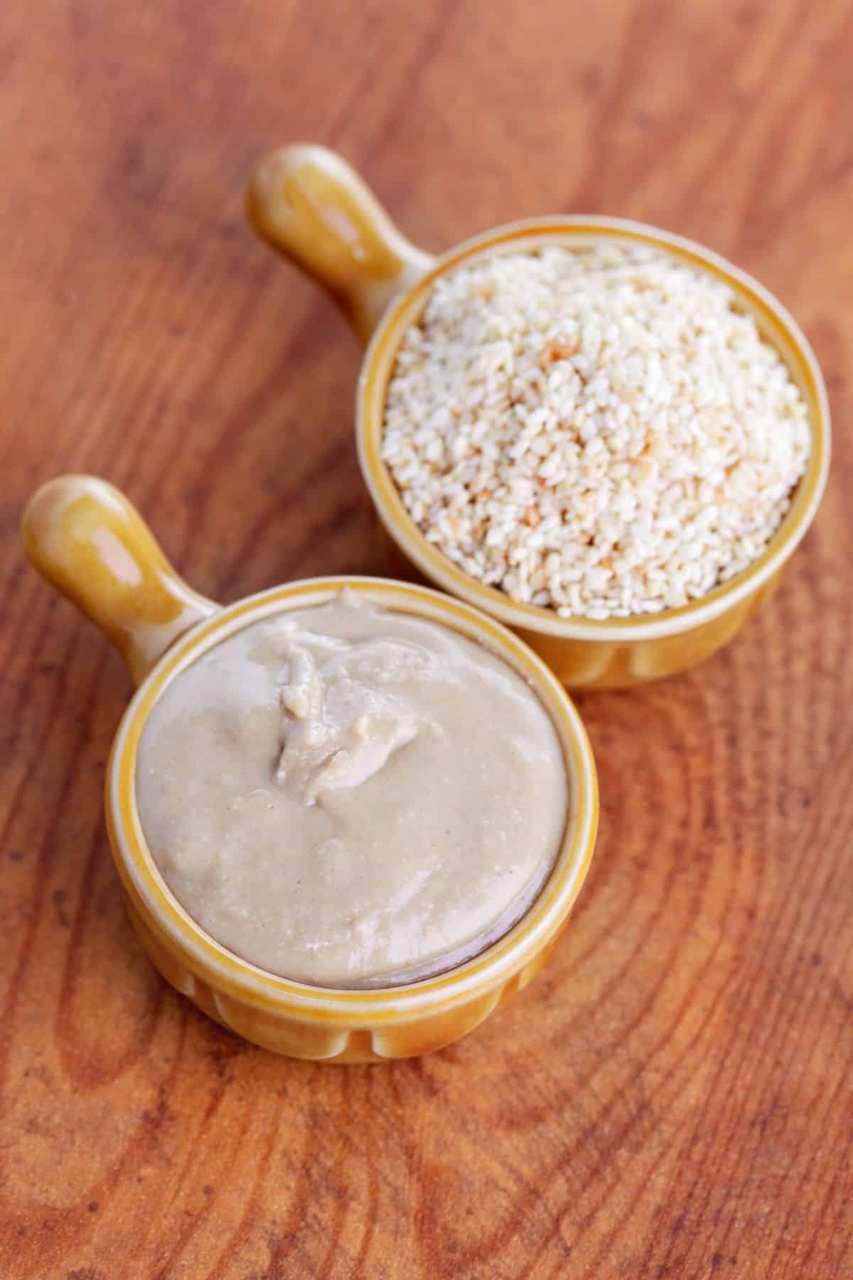 Bowls of sesame seeds and tahini on wooden surface.