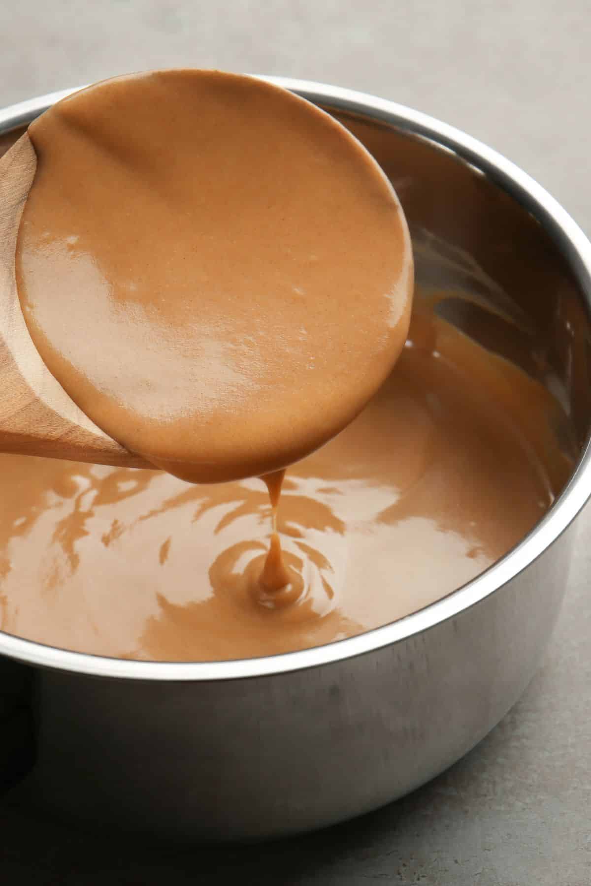 A wooden spoon showing thick turkey gravy over a saucepan.