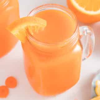 Carrot orange juice in a handled mason jar with an orange slice on the rim.