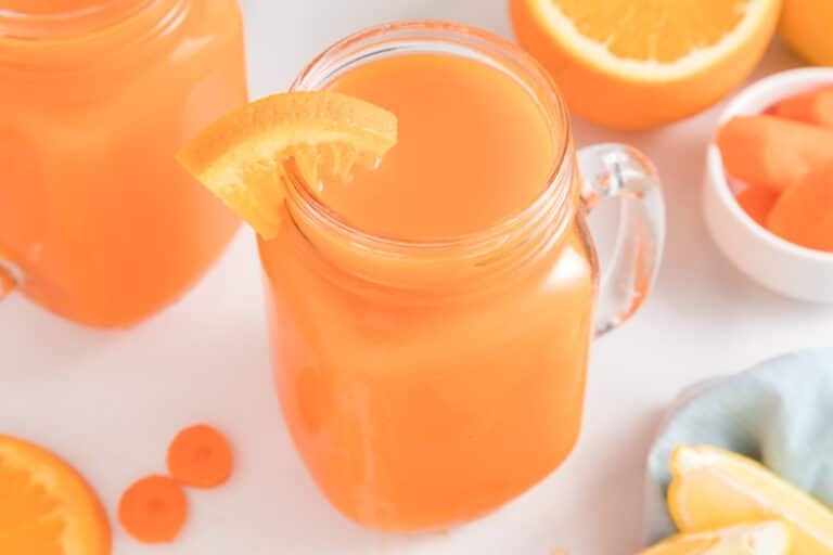 Carrot orange juice in a handled mason jar with an orange slice on the rim.