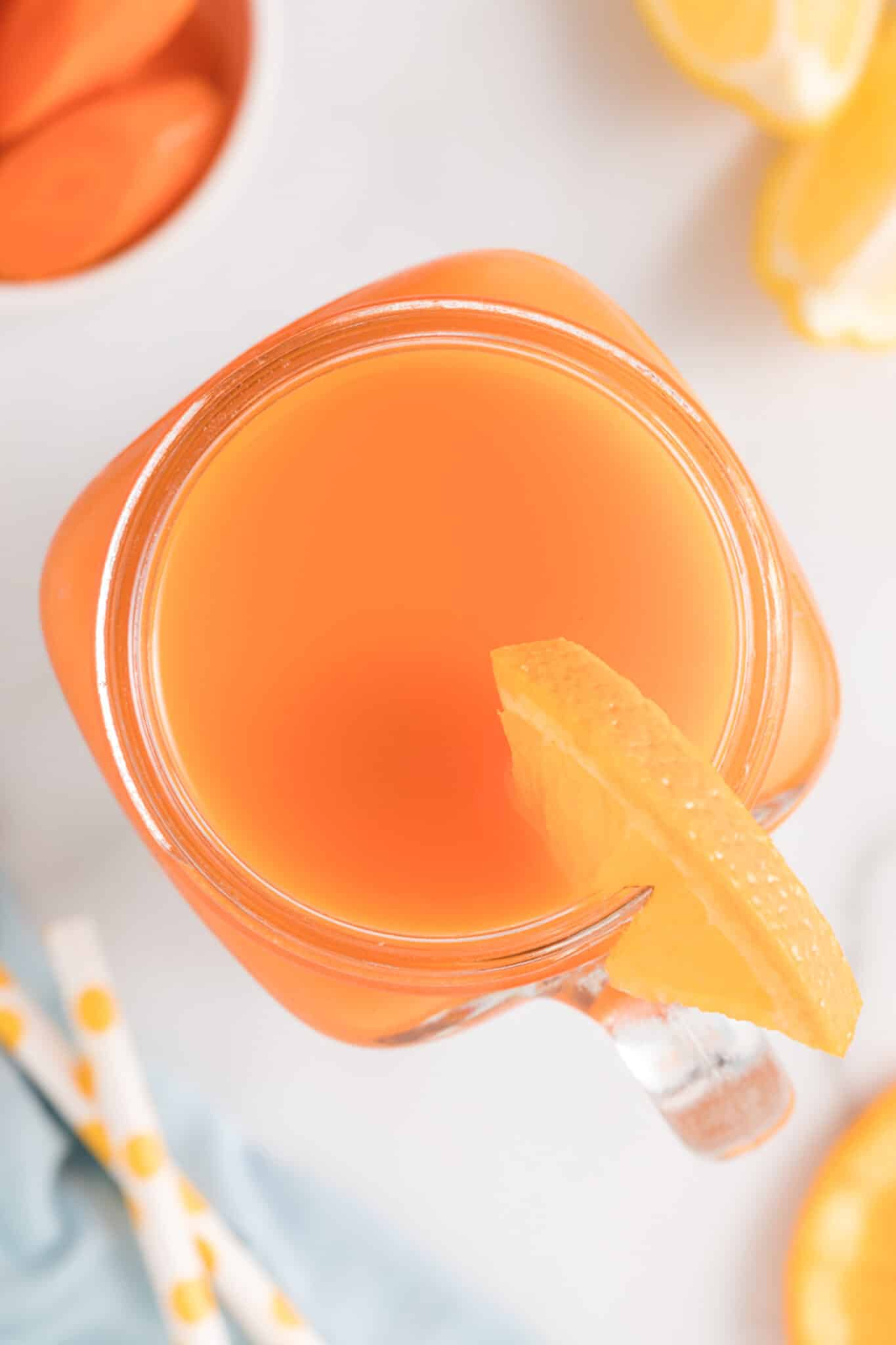 Carrot orange juice in a handled mason jar with an orange slice on the rim.