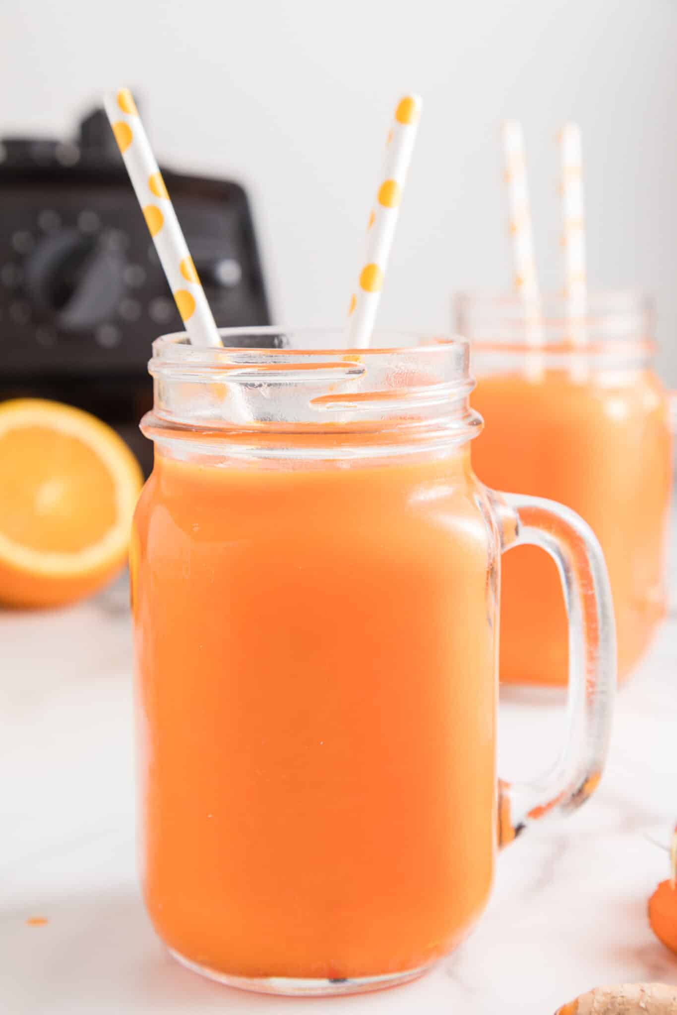 Vitamix carrot juice in a handled mason jar with two paper straws.