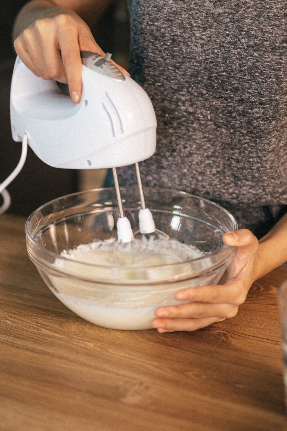A woman using a hand mixer in a glass bowl of frosting.