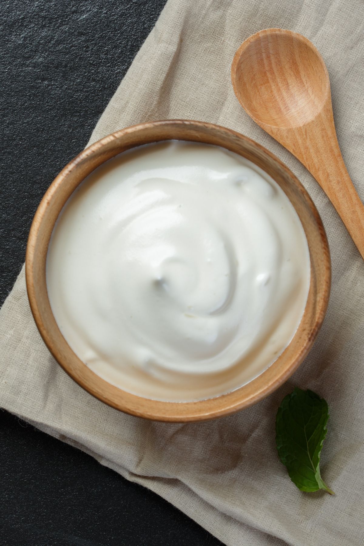 a wooden bowl of yogurt next to a wooden spoon.