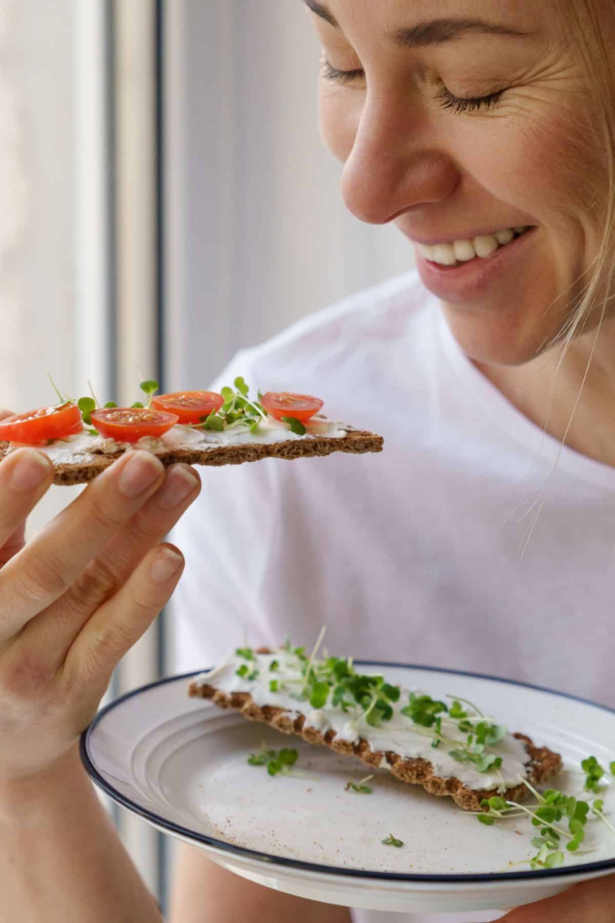 a woman smiling and eating microgreens.