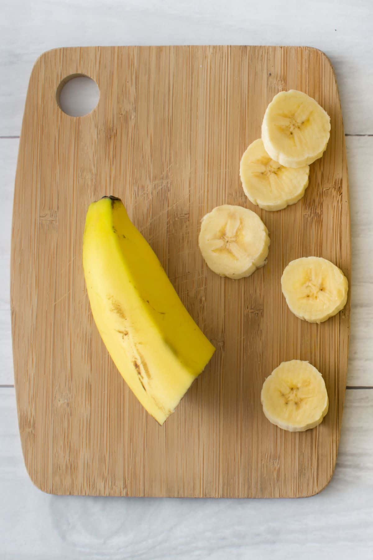 A banana half and slices on a wooden cutting board.