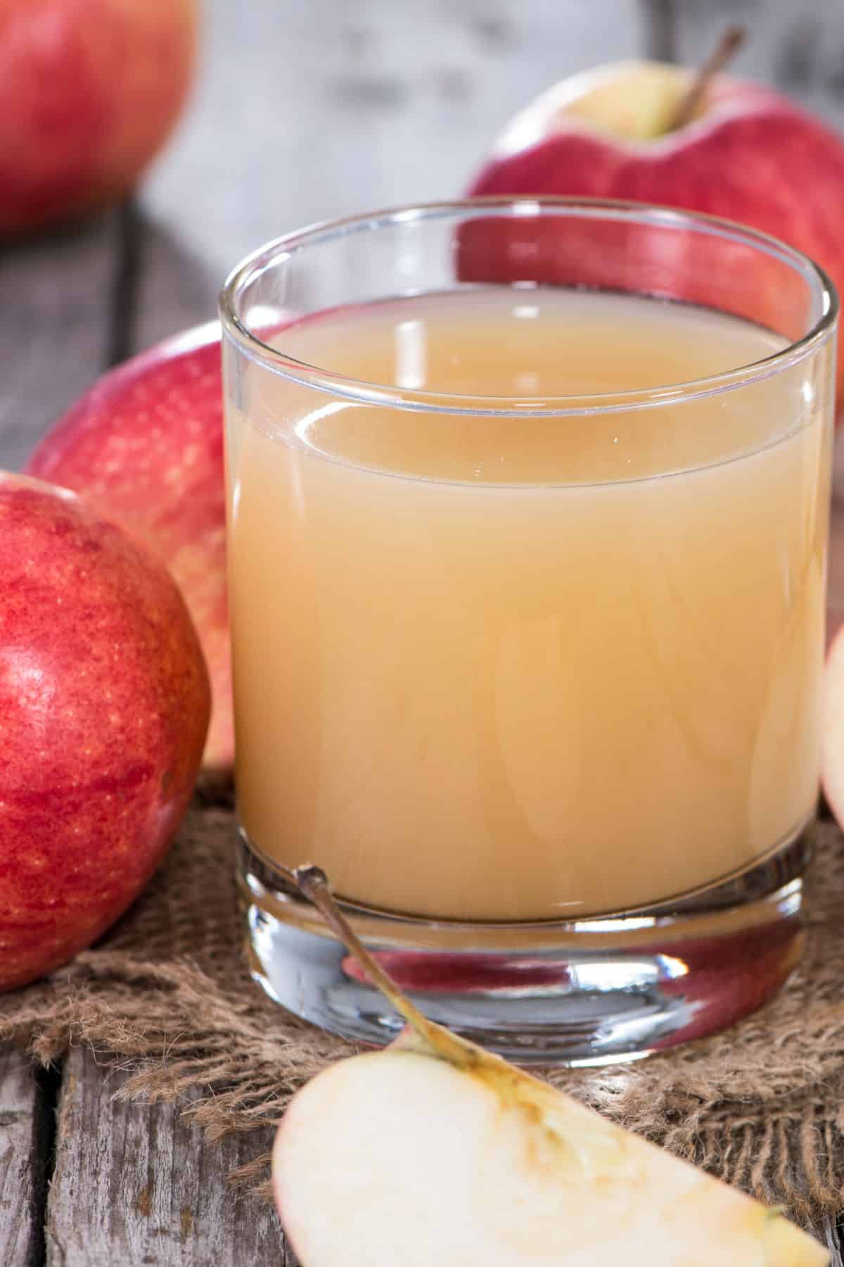 A short glass of apple cider next to fresh whole apples.