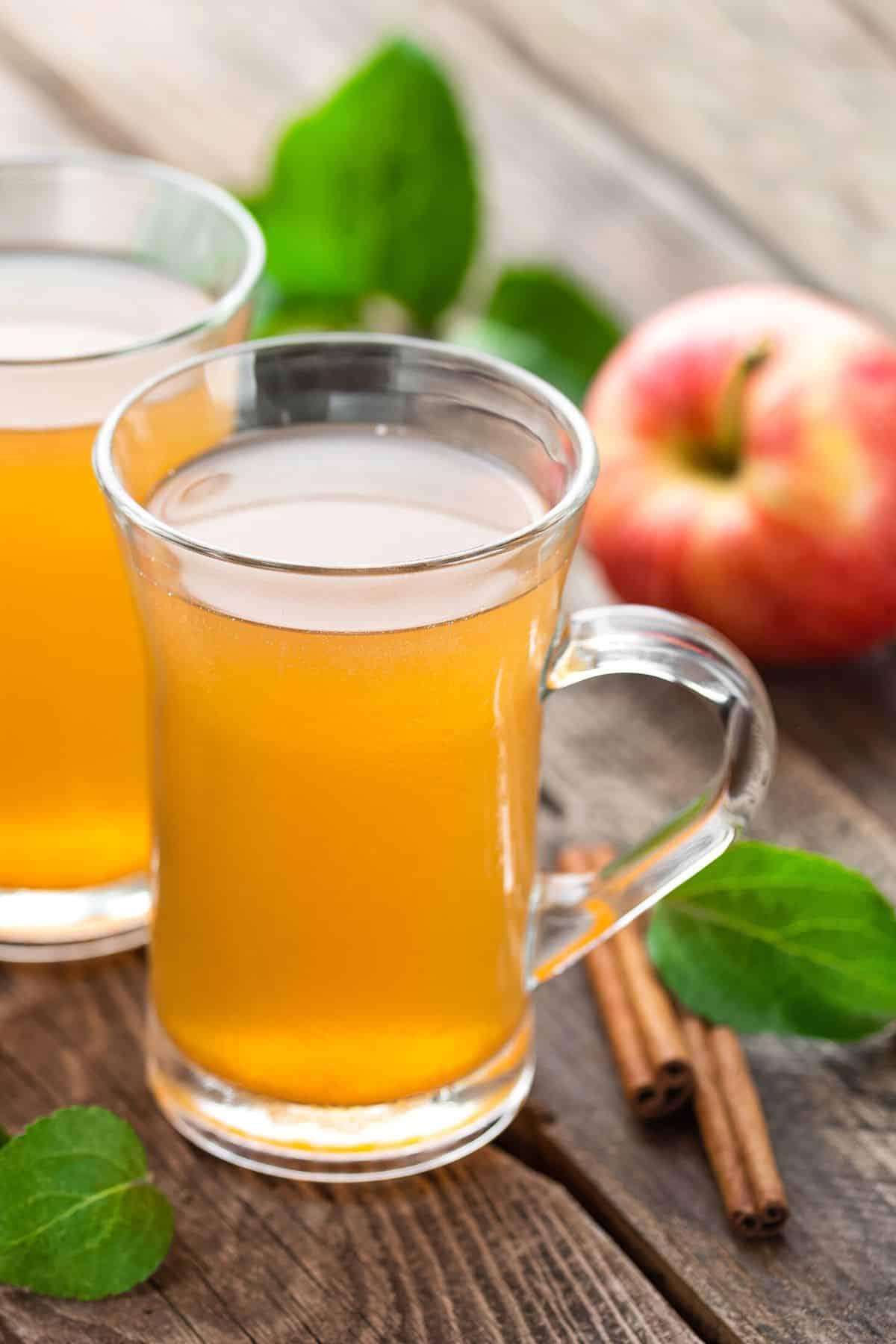Two mugs of apple cider on a wooden table.
