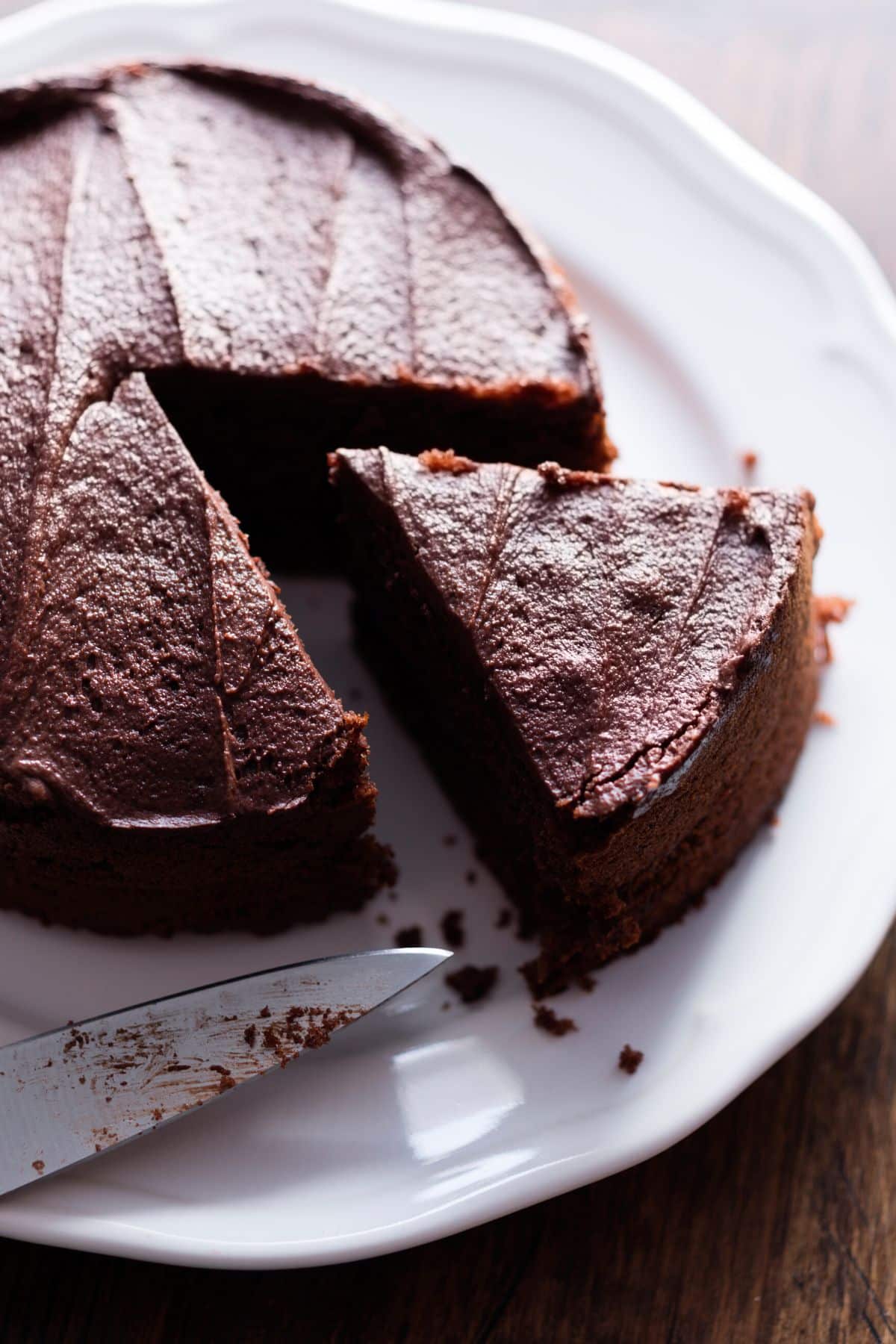 A round dairy-free chocolate cake on a white plate with a slice cut.