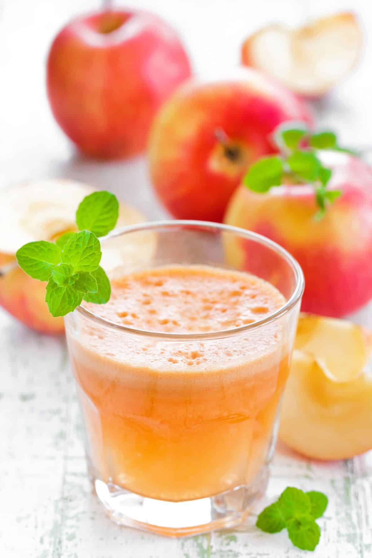 A short glass of freshly squeezed apple juice in front of whole apples.