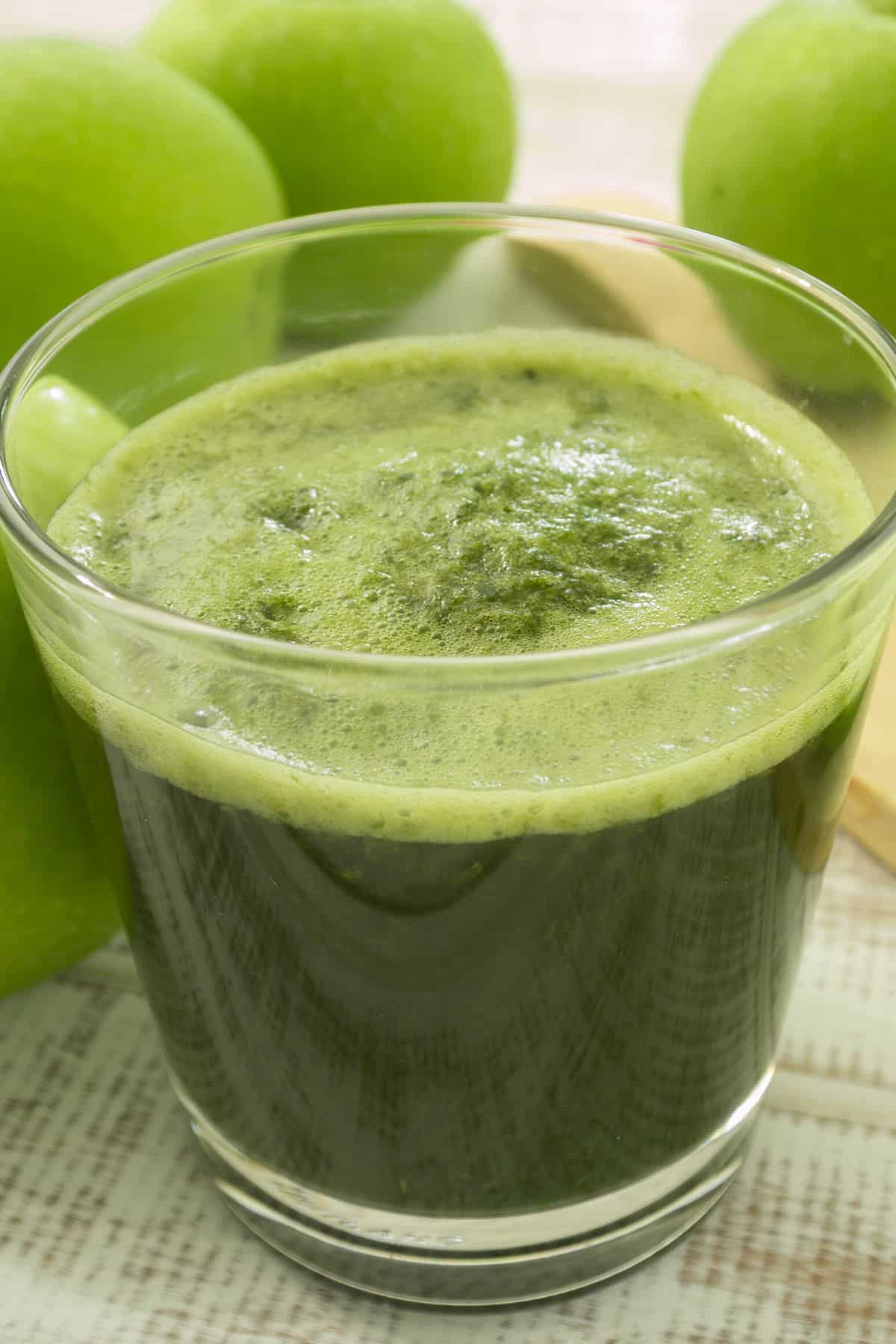 A short glass of green juice on the table with green apples.