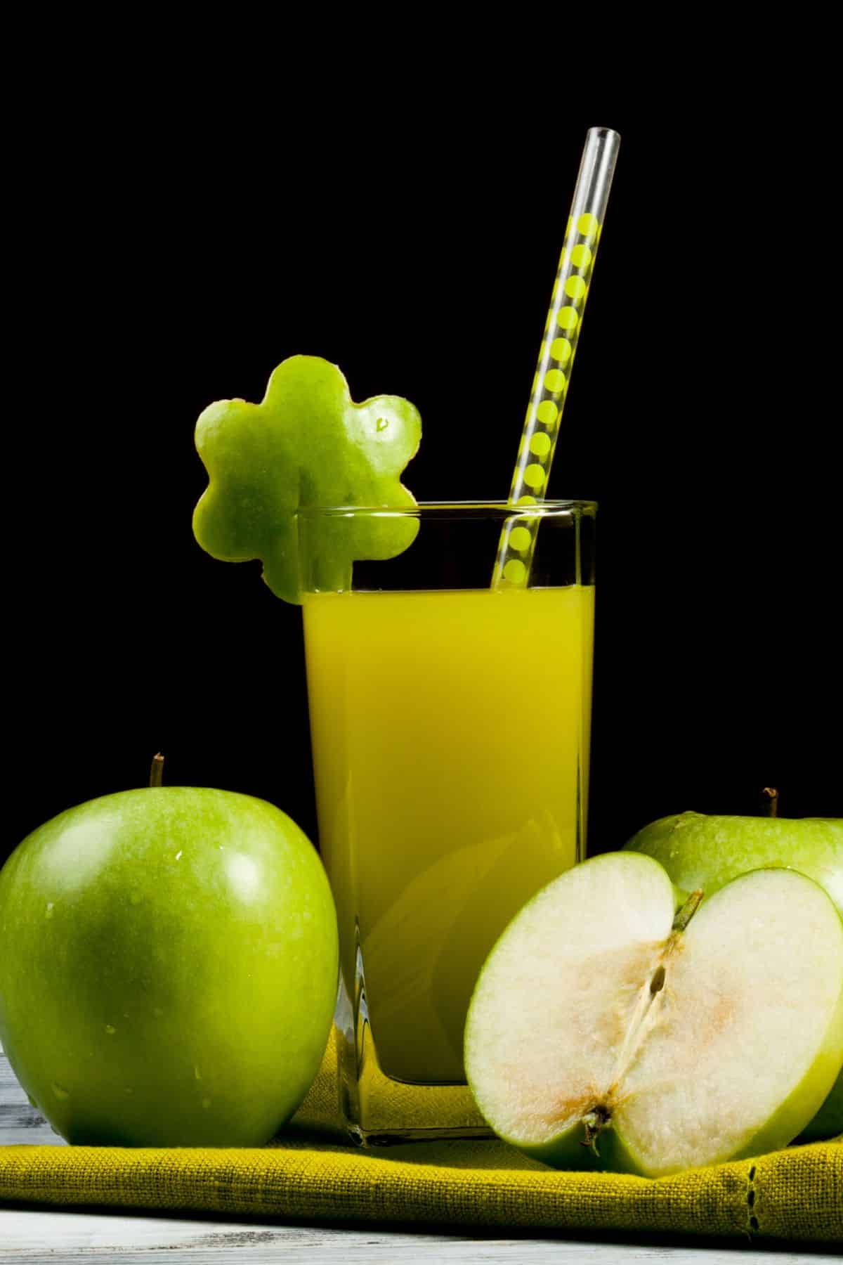 A tall glass of green apple juice with a straw.