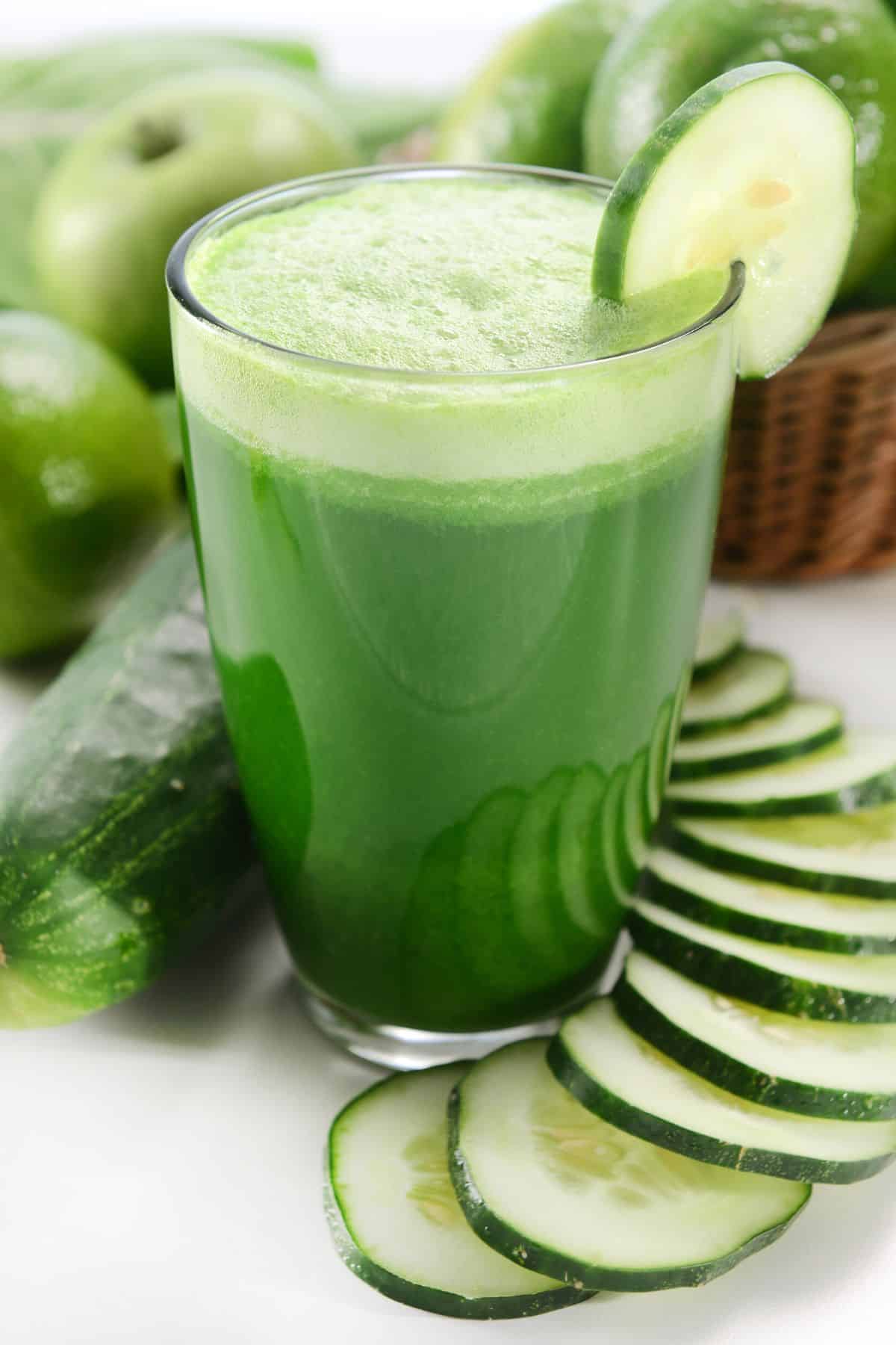 A short glass of green juice on the table with cucumber slices.