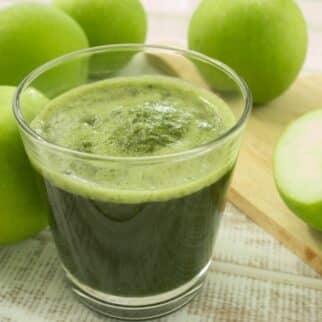 A squat glass of green apple juice on the table with Granny Smith apples.