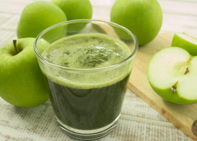 A squat glass of green apple juice on the table with Granny Smith apples.