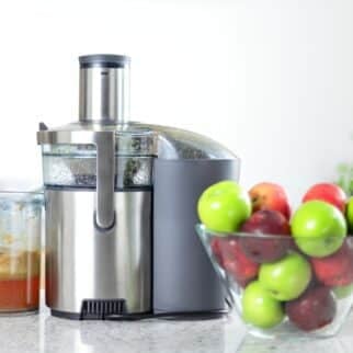 A juicer next to a bowl of red and green apples.