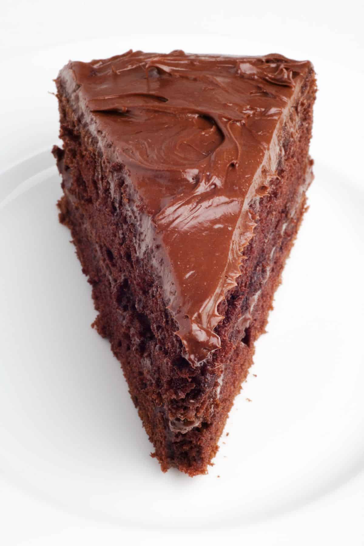 A triangle slice of dairy free chocolate layer cake with frosting.