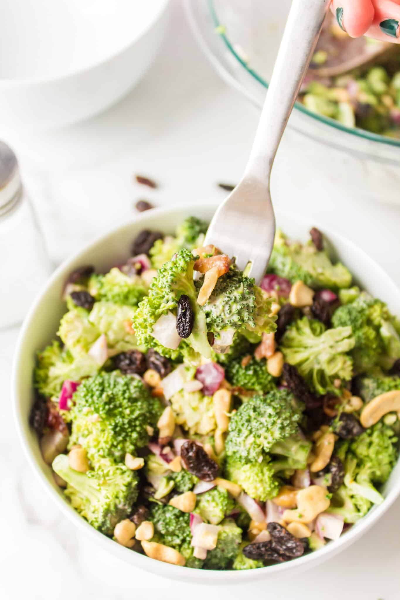 Broccoli crunch salad with raisins and cashews in a white bowl.