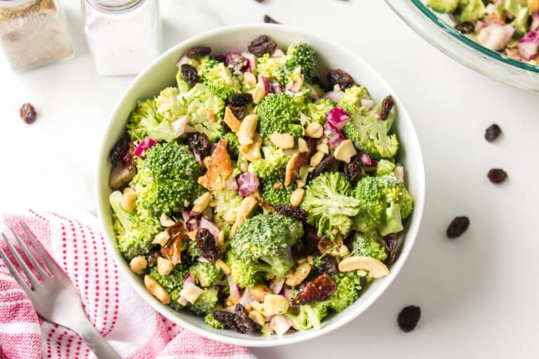 Broccoli crunch salad with raisins and cashews in a white bowl.