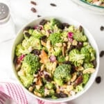 Broccoli crunch salad with raisins and cashews in a white bowl.