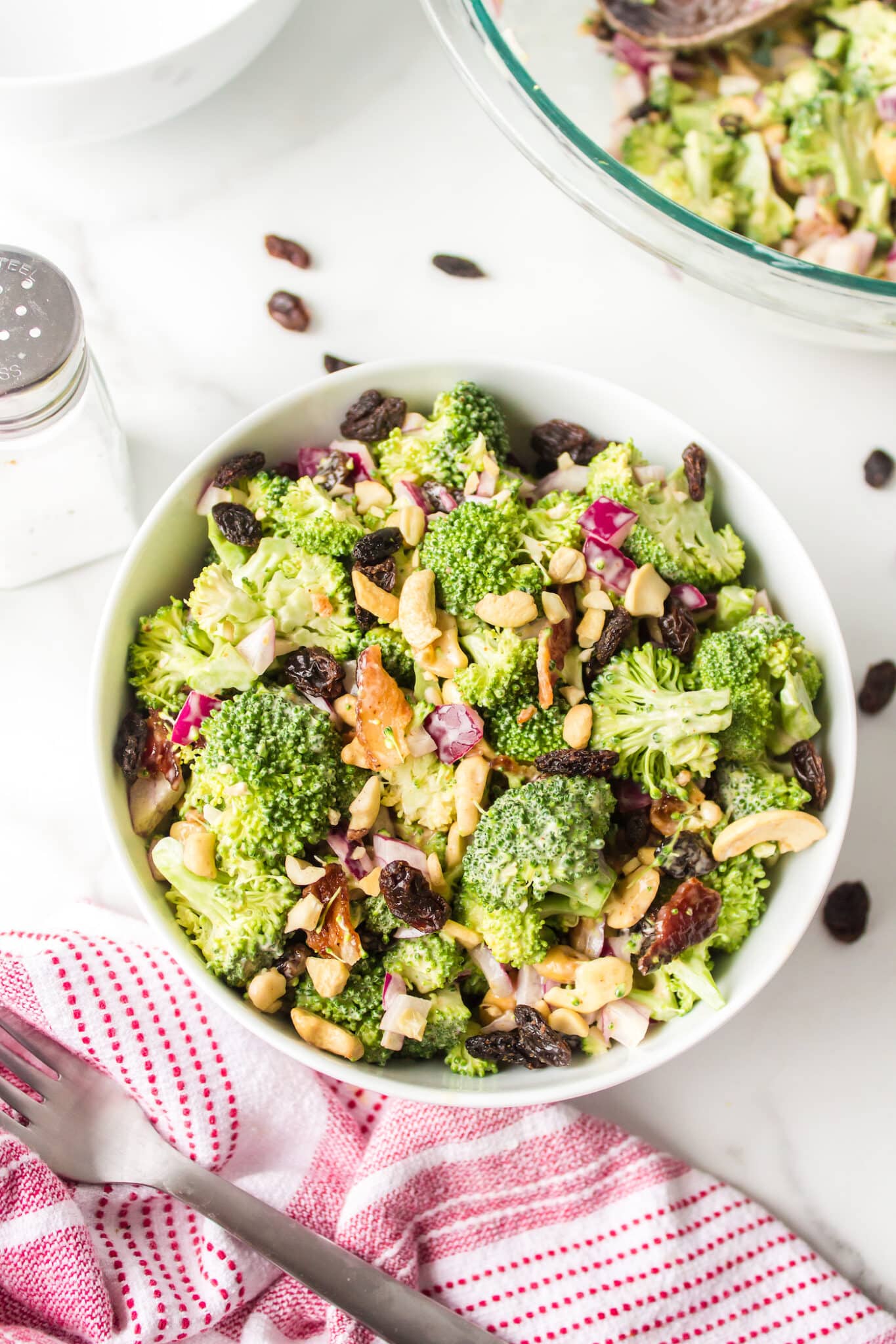 Broccoli crunch salad with raisins and cashews in a white bowl.