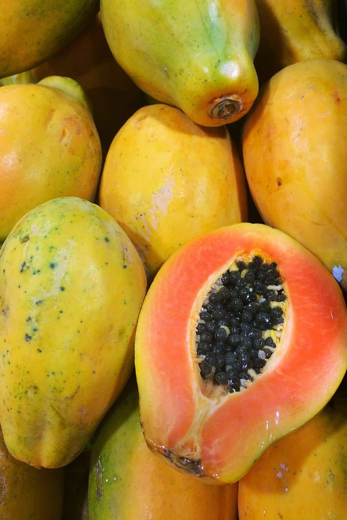 Fresh papaya in a pile with one sliced in half.