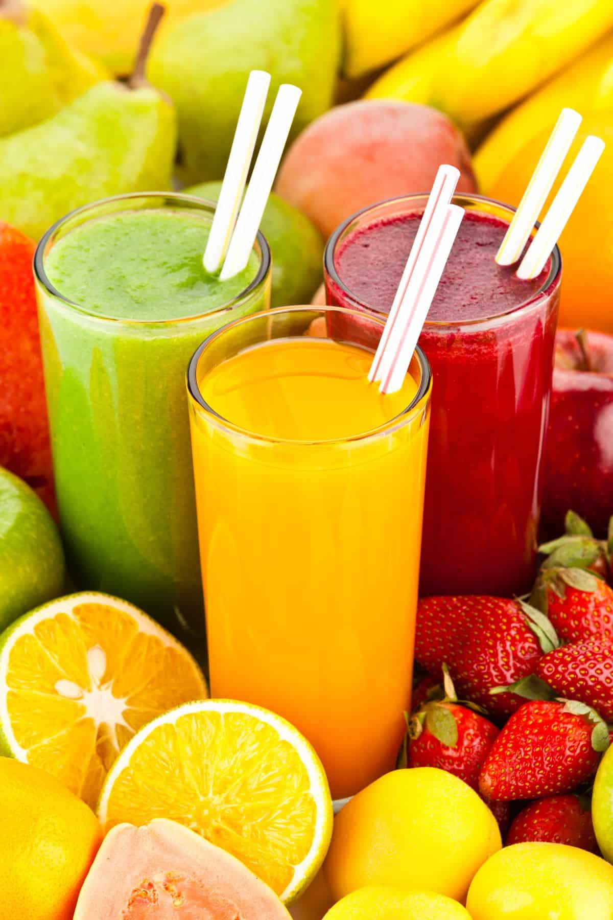 three cups of juice with straws surrounded by fruits.