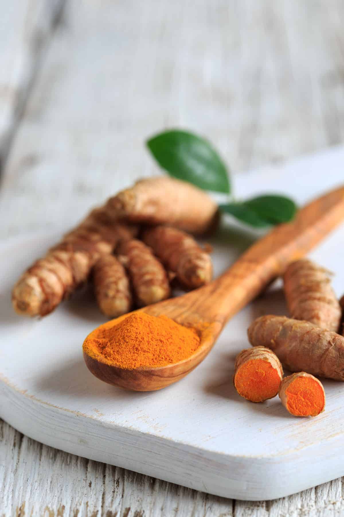 turmeric on a wooden spoon, surrounded by whole pieces of turmeric.