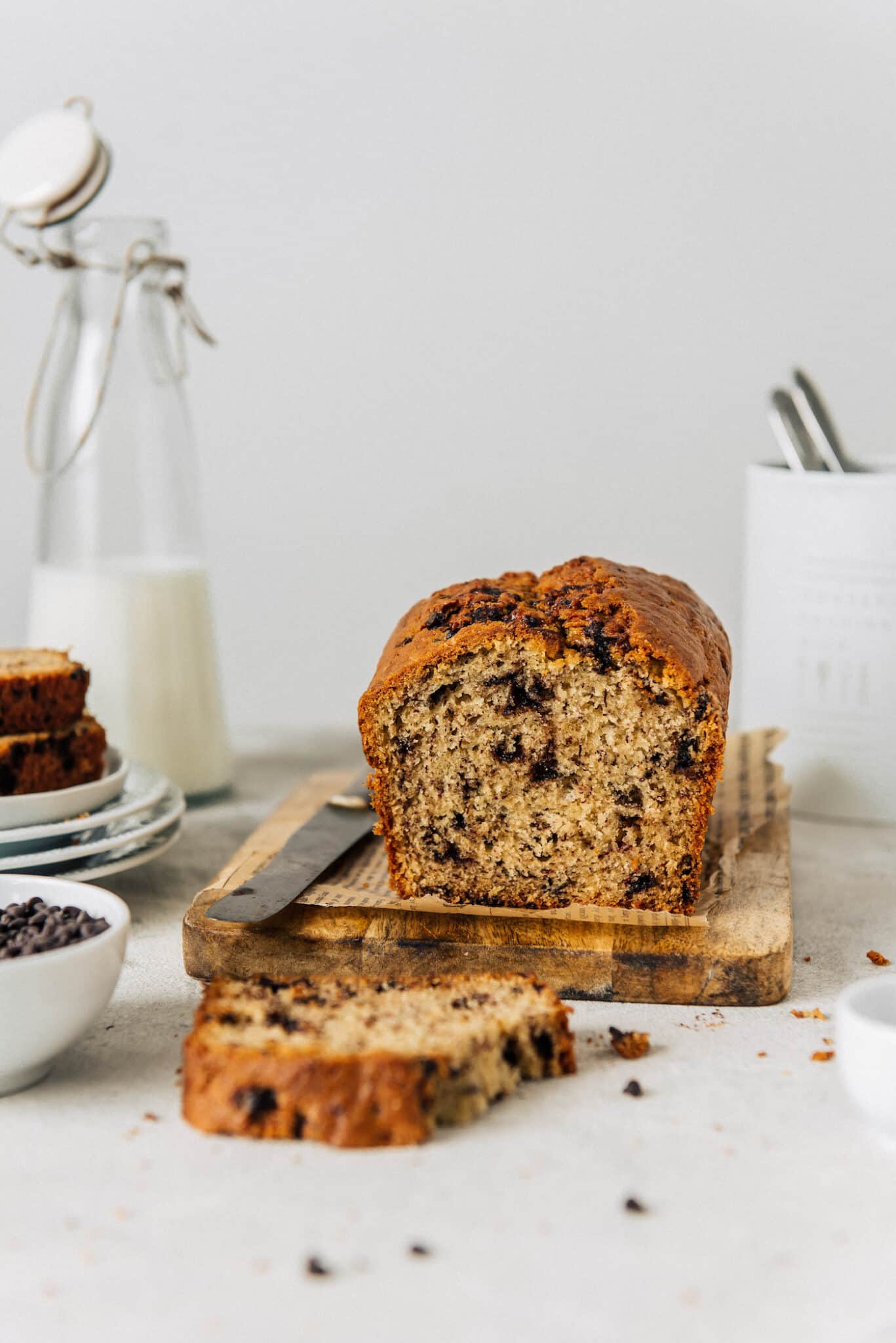 loaf of dairy-free banana bread with chocolate chips on a cutting board with knife.