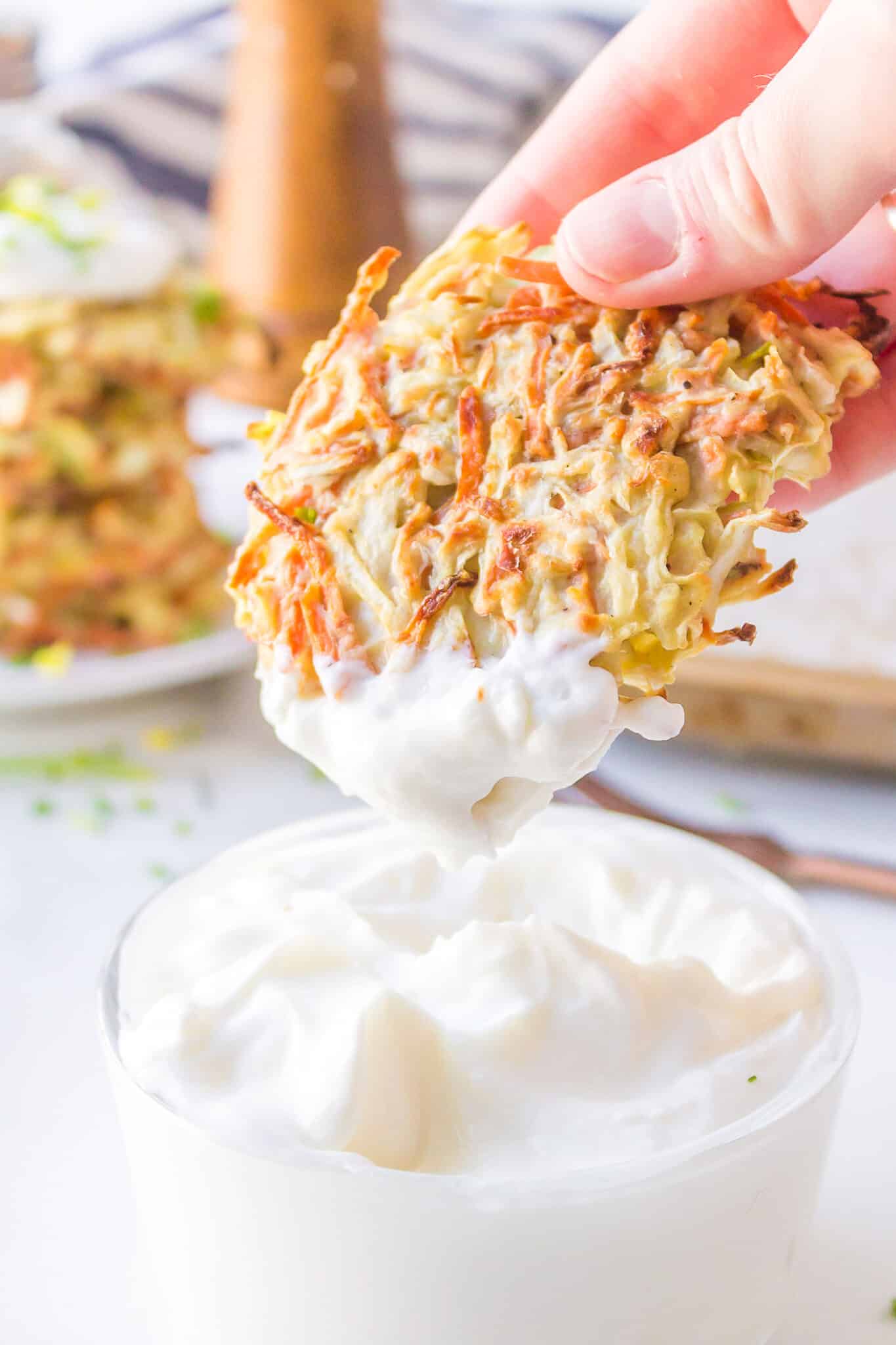 A hand dipping a baked cabbage fritter into sour cream.
