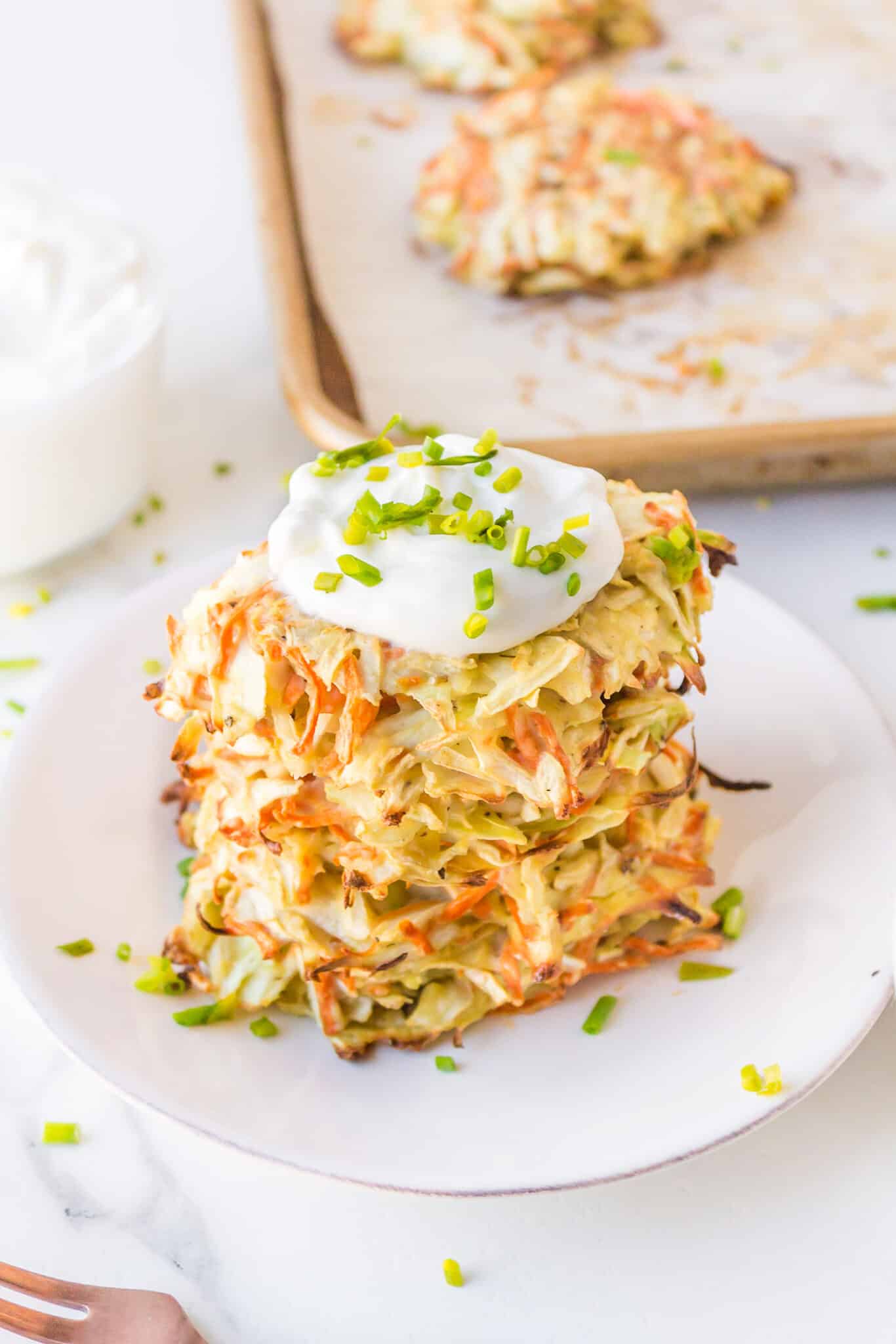 Cabbage fritters stacked on a white plate, topped with sour cream.