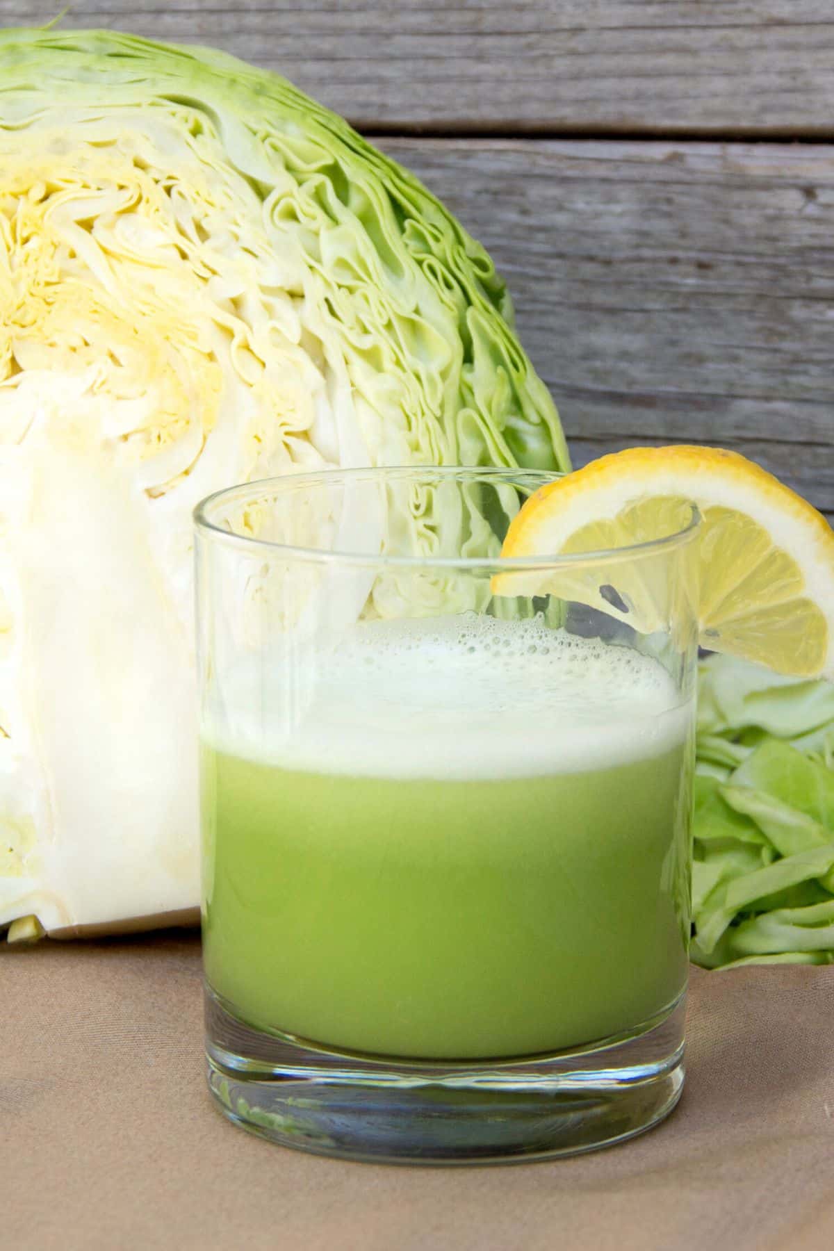 A glass of cabbage juice in front of a halved cabbage head.
