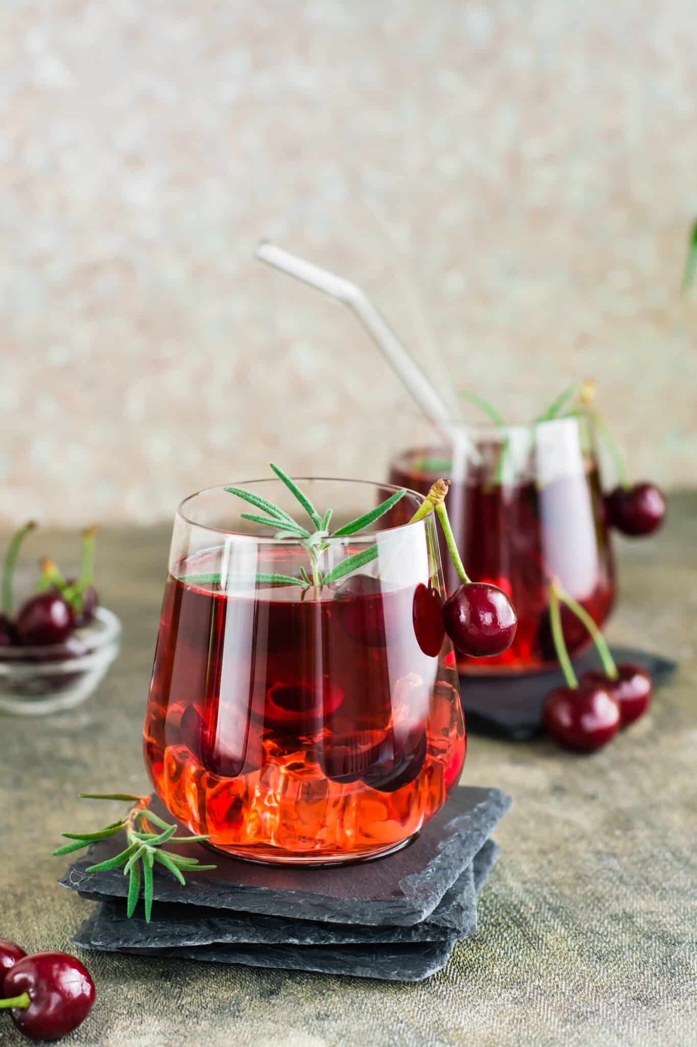 two glasses of pretty cherry mocktail garnished with cherries and rosemary.