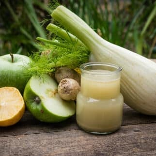 A glass of fennel juice next to fennel, apple, and ginger.