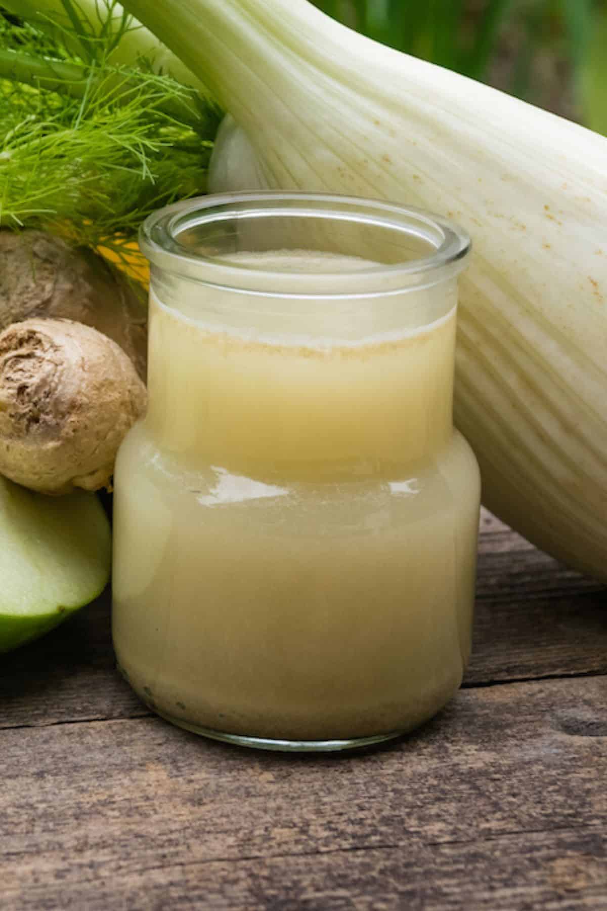 A glass of fennel juice next to fennel, apple, and ginger.