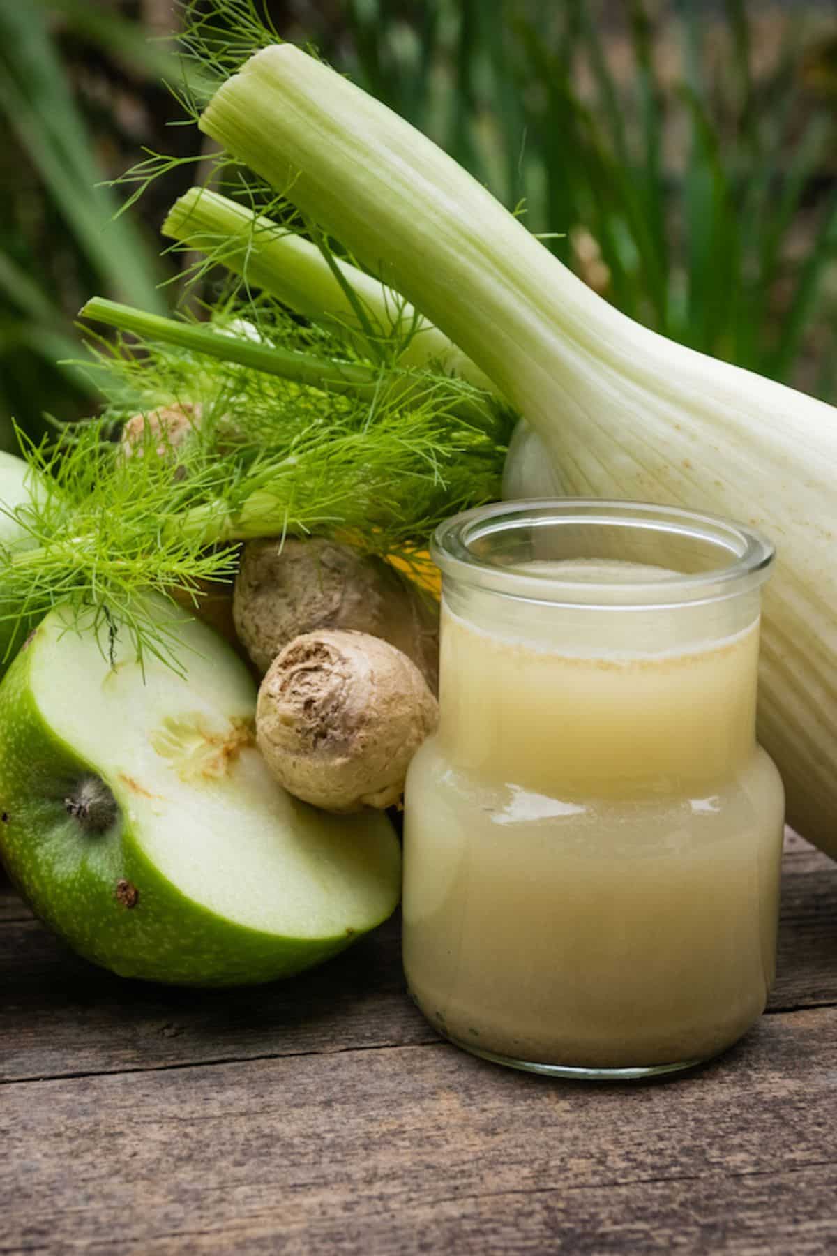 A glass of fennel juice next to fennel, apple, and ginger.