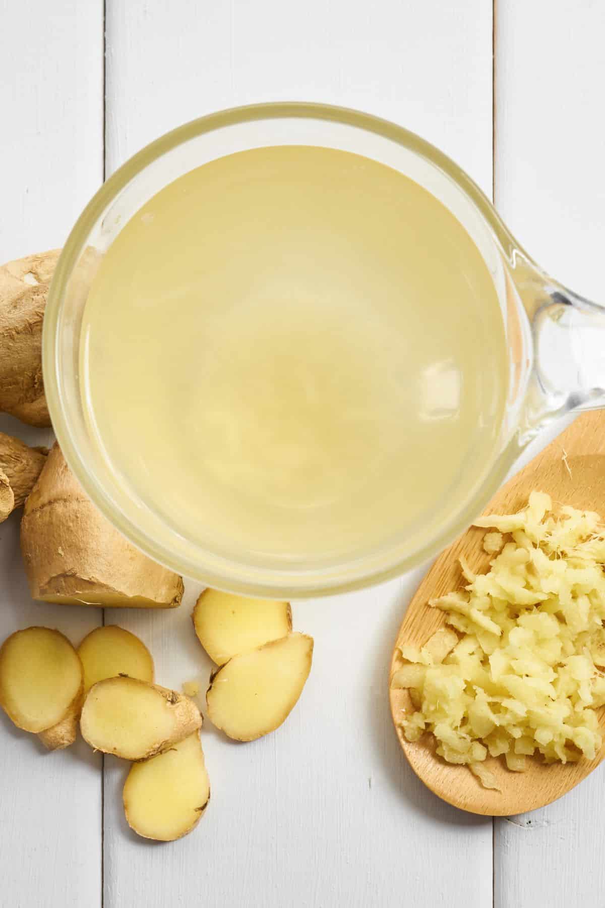 Ginger juice and fresh ginger on a white wooden surface.