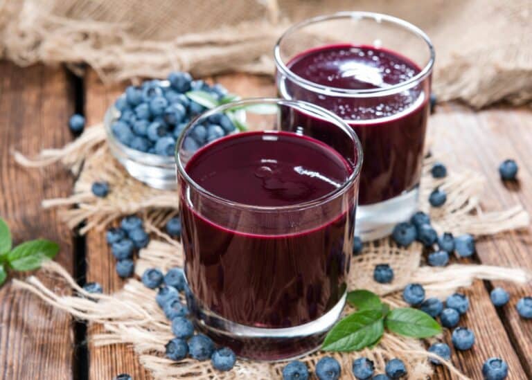 Two short glasses filled with blueberry juice on a table with fresh blueberries.