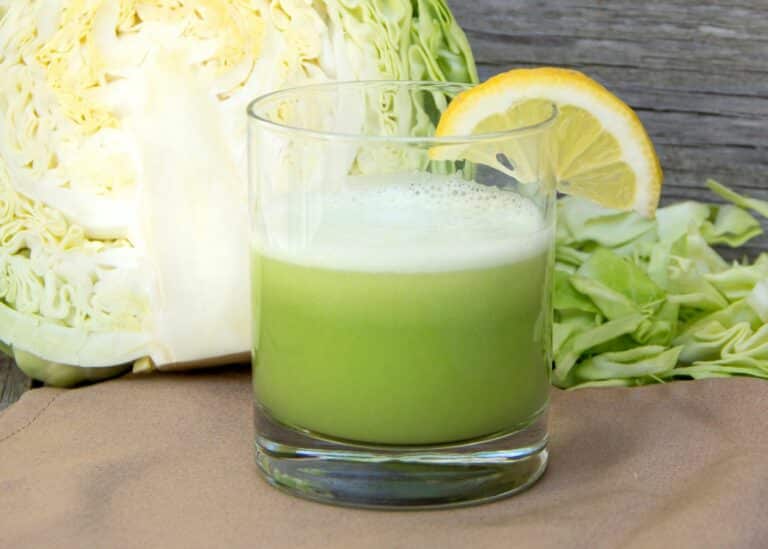 A glass of cabbage juice in front of a halved cabbage head.