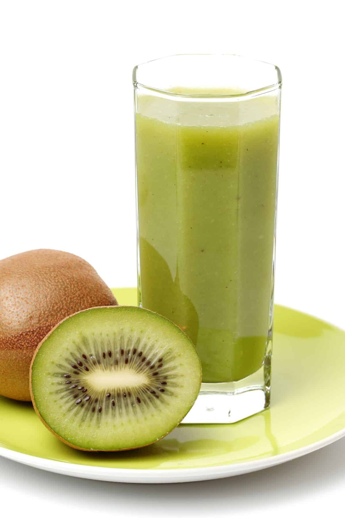 A tall glass of kiwi juice next to two fresh kiwi.