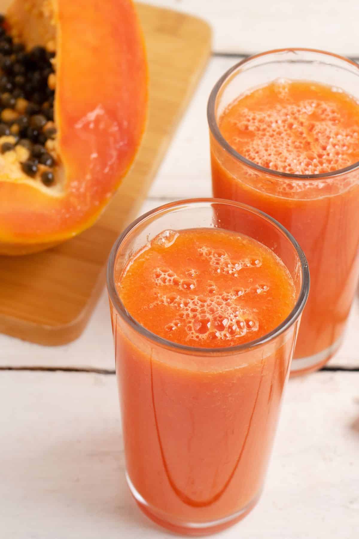 Two glasses of papaya juice next to a fresh papaya.