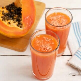 Two glasses of papaya juice next to a fresh papaya.