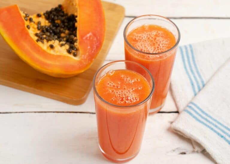 Two glasses of papaya juice next to a fresh papaya.