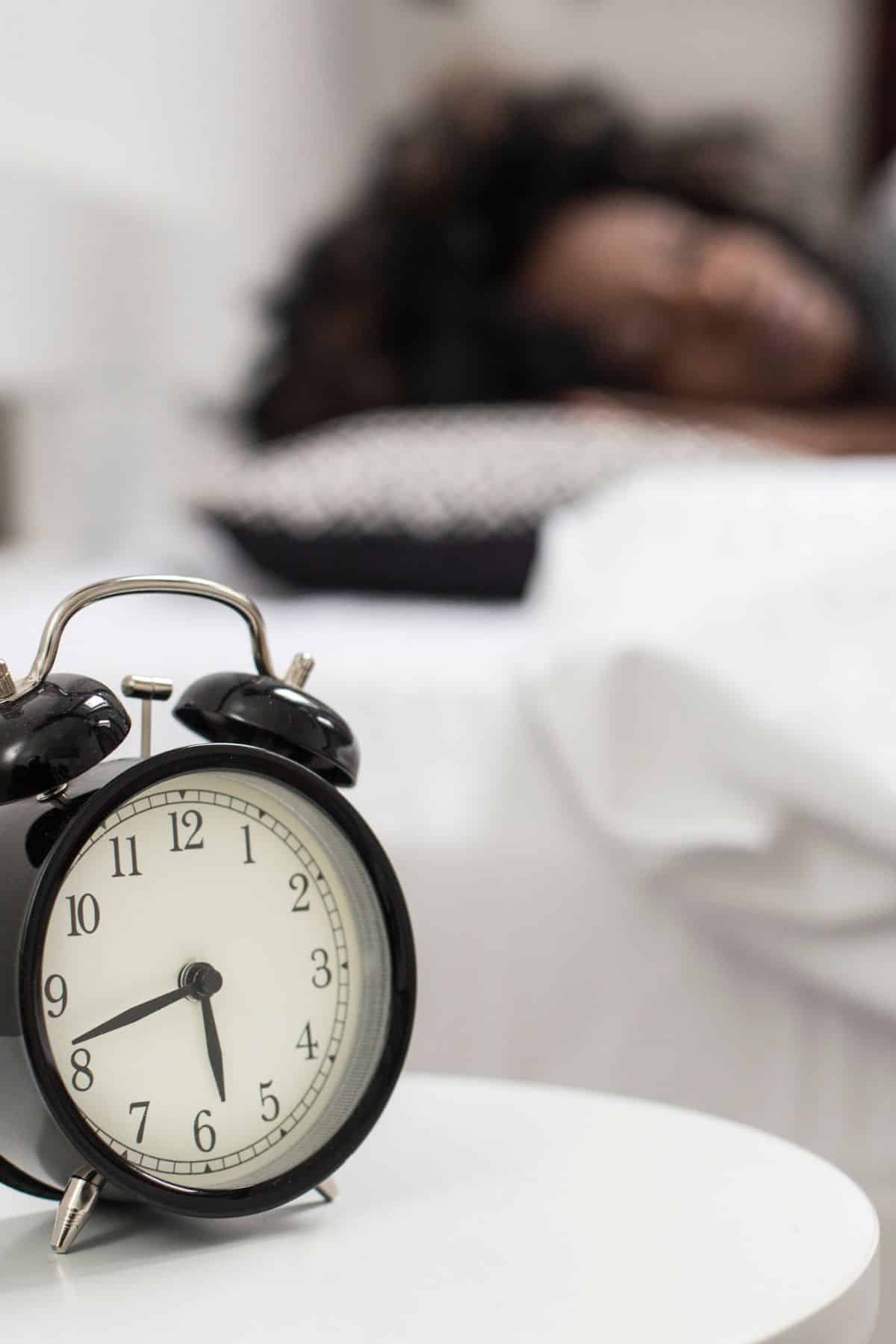 an alarm clock in front of a woman sleeping in the bed.