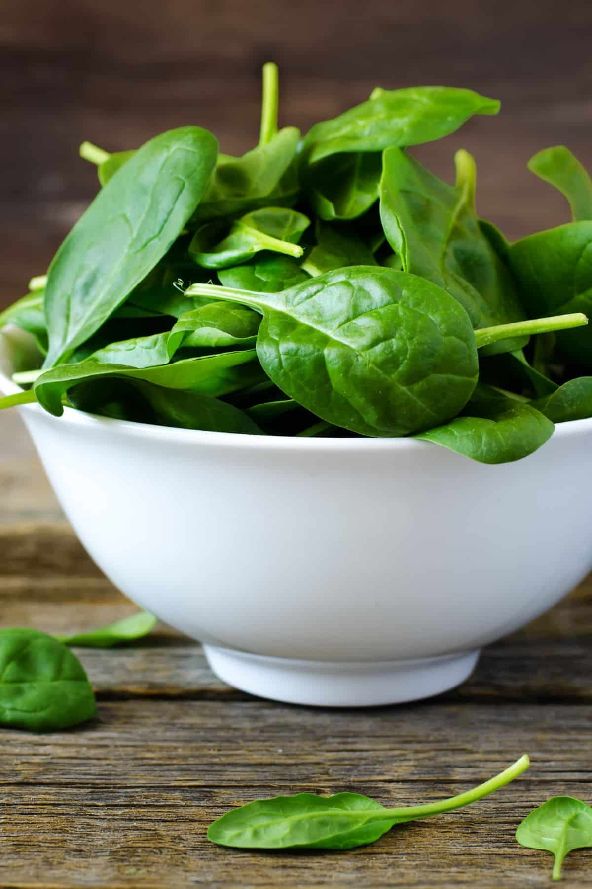 A white bowl filled with fresh spinach leaves.
