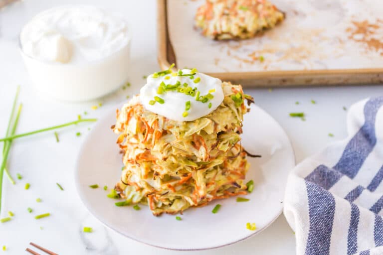 Cabbage fritters stacked on a white plate, topped with sour cream.