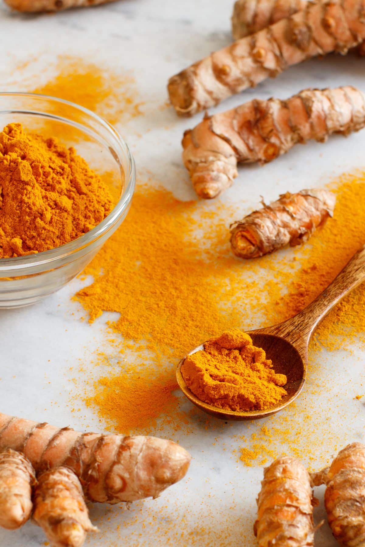 Fresh turmeric root and powdered turmeric on a white surface.