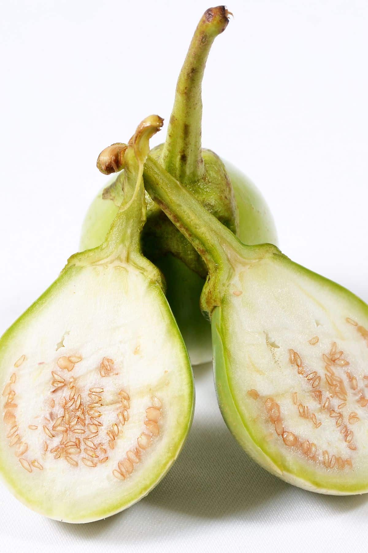 a sliced open Thai eggplant leaning against a whole Thai eggplant.